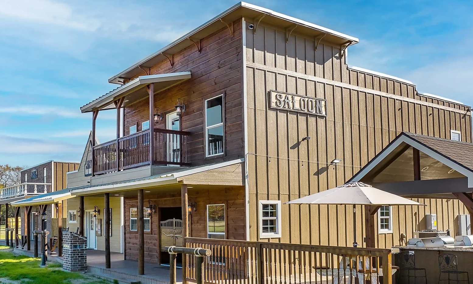 A two-story building designed as a Western-style saloon with wood siding, a balcony, and a wooden deck with an umbrella.