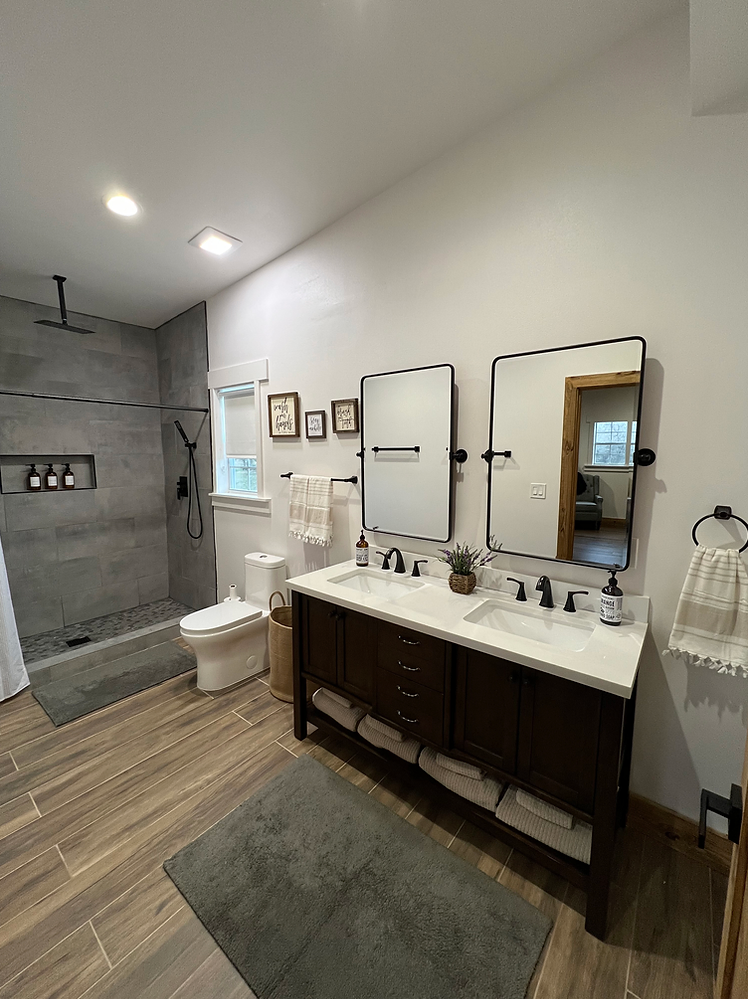 Modern bathroom with a dual-sink vanity, two mirrors, tiled walk-in shower, and wood-look tile flooring.