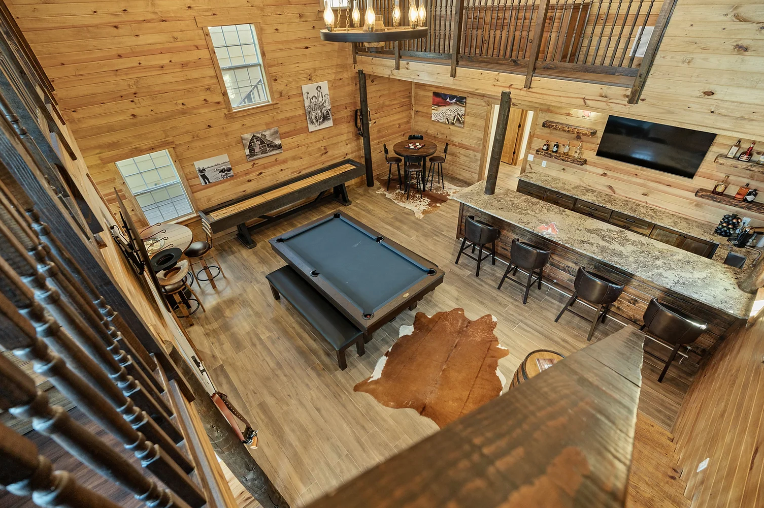 A high-angle view of a rustic game room featuring a pool table, a bar with stools, and wooden walls.