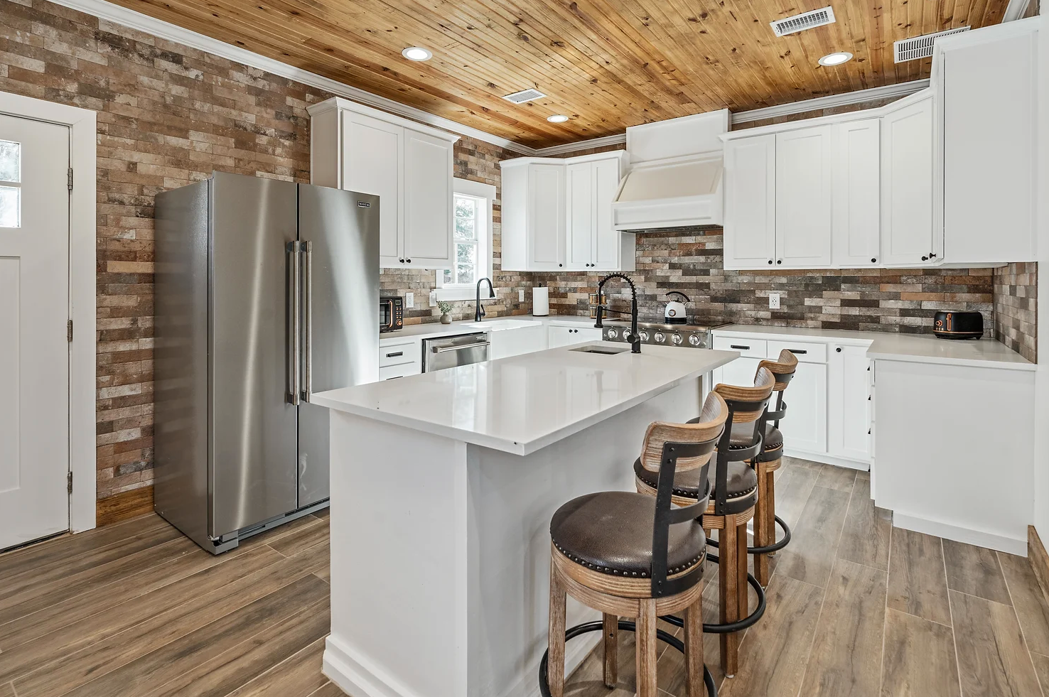 A kitchen featuring white cabinets, a stone backsplash, stainless steel appliances, a wood ceiling, and a central island.