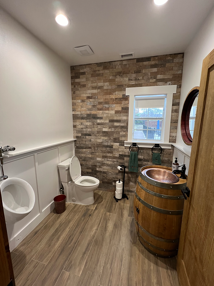 A rustic bathroom featuring a stone accent wall, a wooden barrel vanity with a copper sink, a toilet, and a urinal.