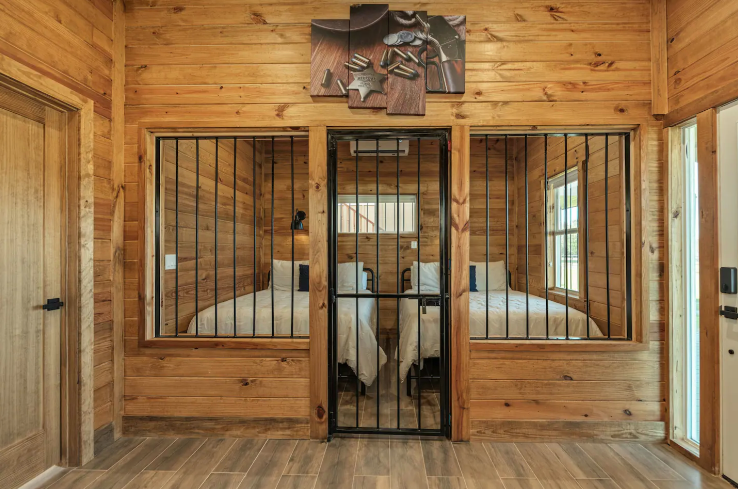 A rustic room with wood paneling features two glass-enclosed sleeping areas separated by a central metal-barred door.