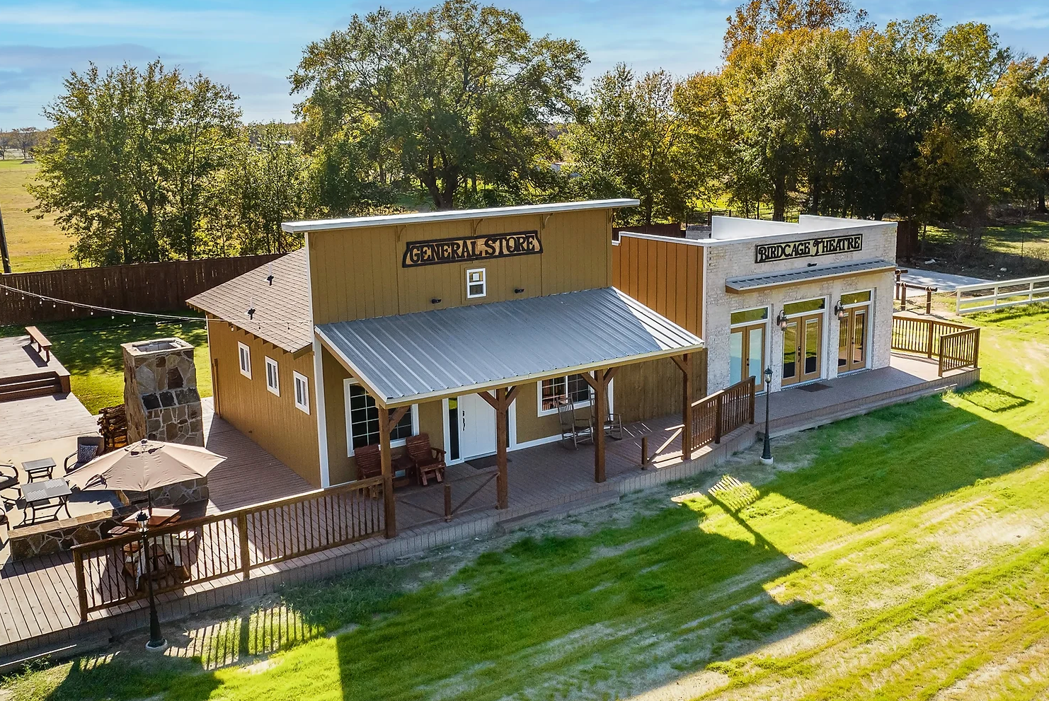 An aerial view of a rustic, Old West-style building with a covered porch and patio, set against a background of trees.
