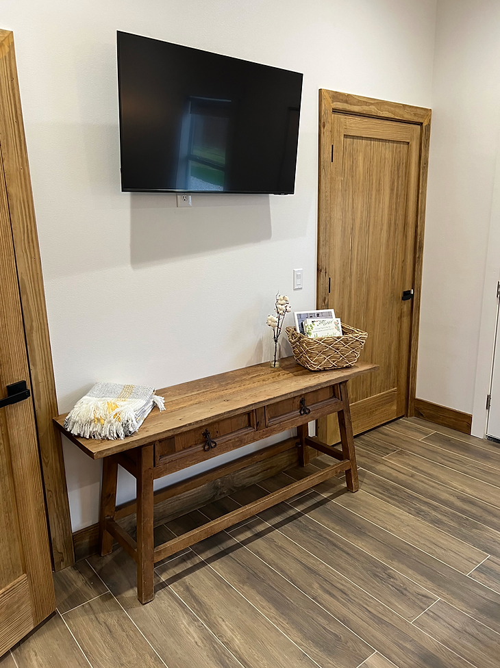 A wall-mounted TV hangs above a wooden console table with a basket and folded throw blanket on a wood-look floor.