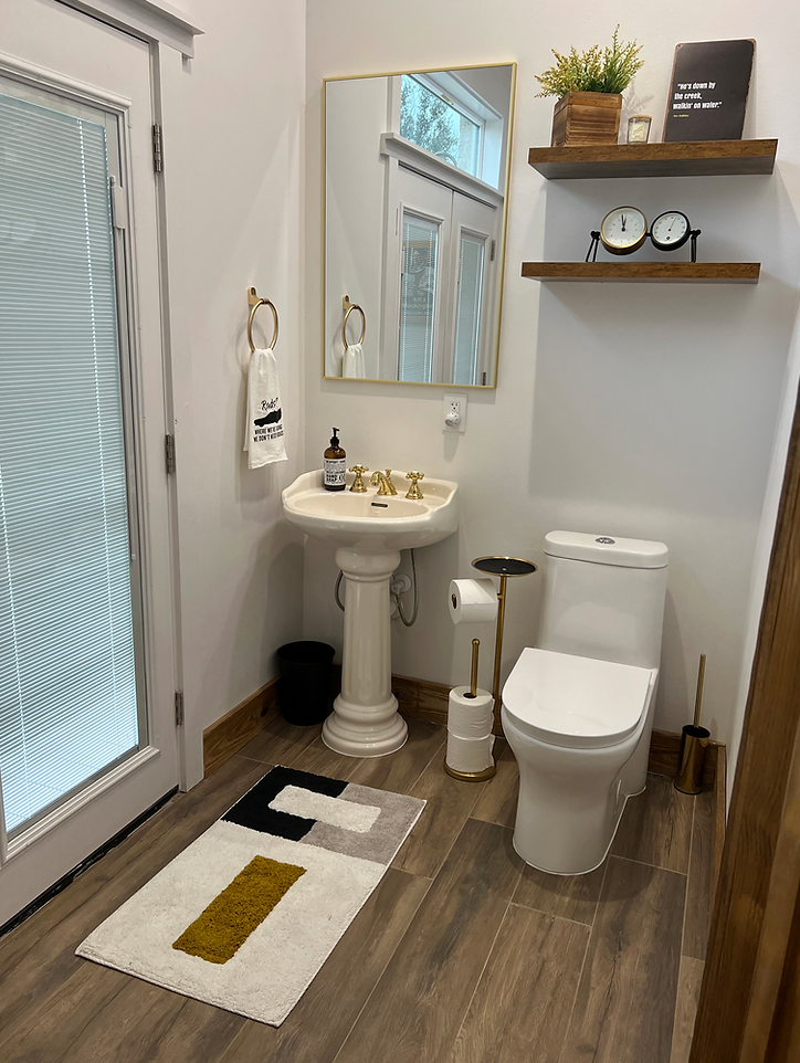 A bright, modern powder room with wood flooring, a pedestal sink, a white toilet, and two floating shelves on the wall.