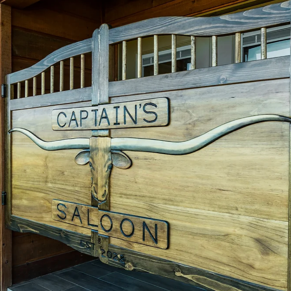 Wooden saloon doors with a sign reading “Captain’s Saloon” and a decorative rifle mount