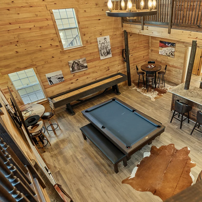 High-angle view of a rustic game room with a pool table, shuffleboard, dining table, and a brown cowhide rug.