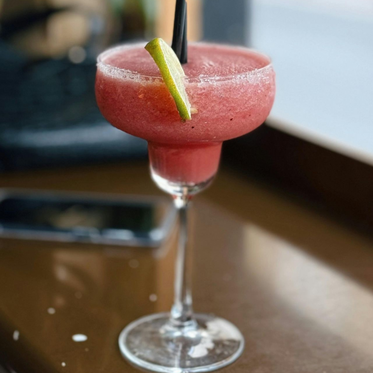 Pink cocktail in a stemmed glass with a lime garnish on a wooden table
