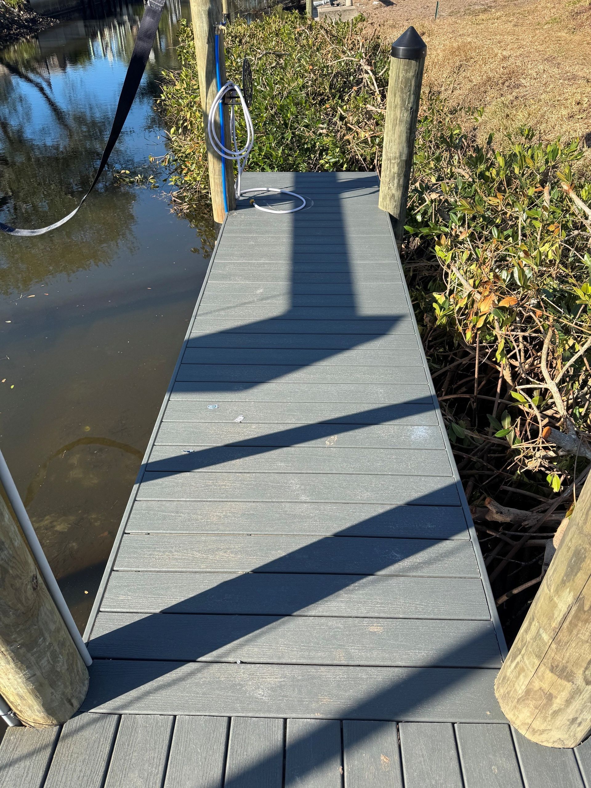 Narrow wooden dock over water, with rope handrails and posts casting shadows.