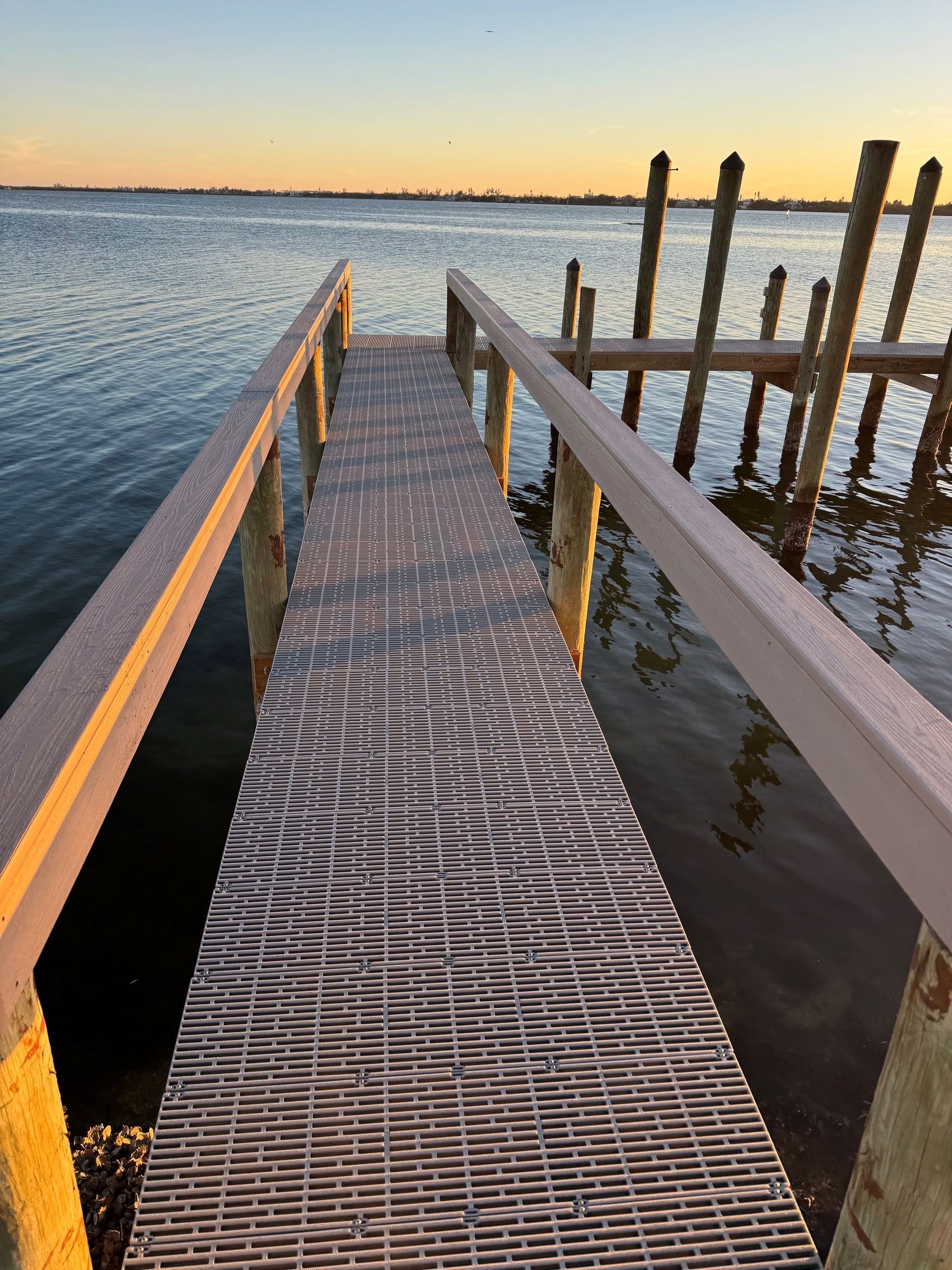 Wooden dock at sunset over calm water, with weathered posts and a netted walkway. Wooden dock at sunset over calm water, with weathered posts and a netted walkway.