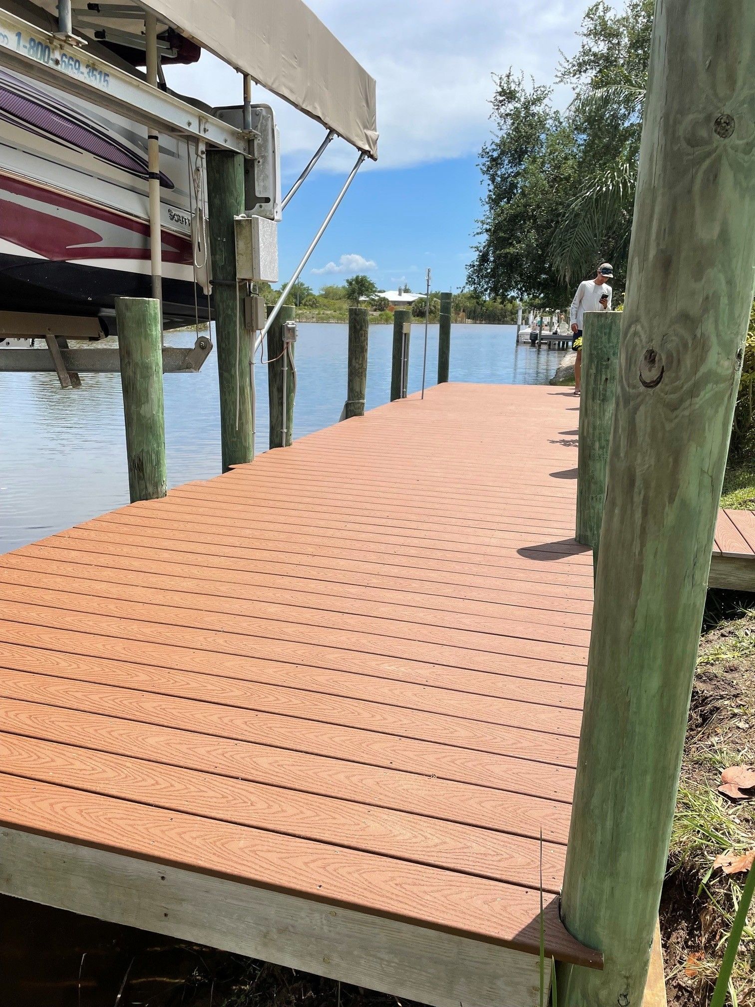 Wooden dock walkway beside calm water, with posts and a boat lift on a sunny day.
