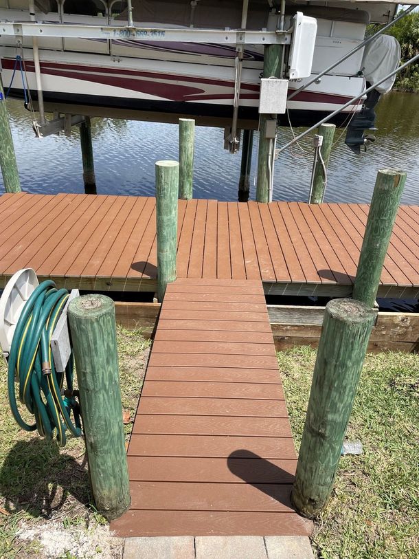 Wooden dock with a hose reel on the left, leading to a marina with boats on calm water. Wooden dock with a hose reel on the left, leading to a marina with boats on calm water.