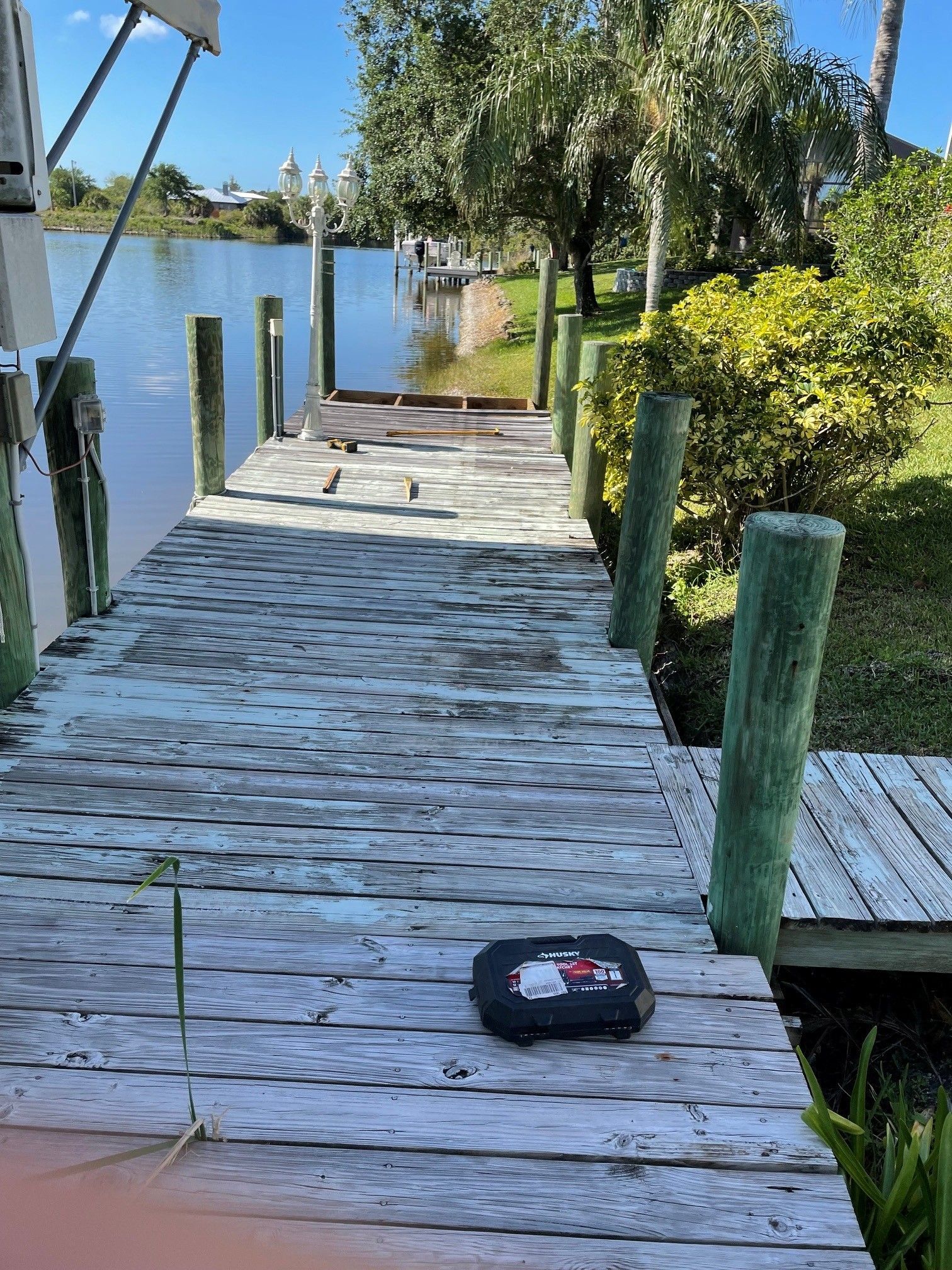 Weathered wooden dock by a calm lake, with a small black case on the planks and trees along the shore.