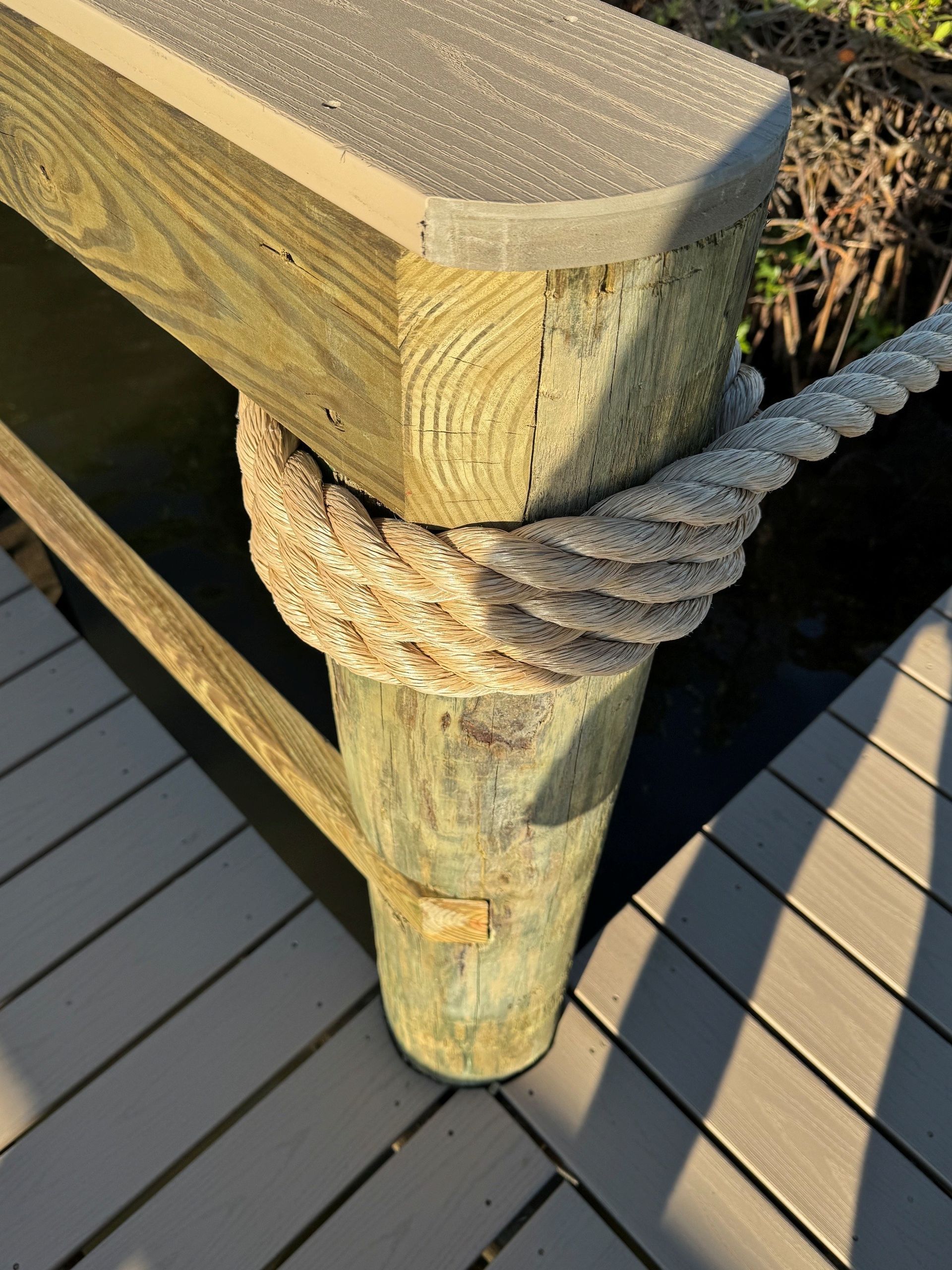 Wooden dock railing post wrapped with thick rope beside a gray deck. Wooden dock railing post wrapped with thick rope beside a gray deck.