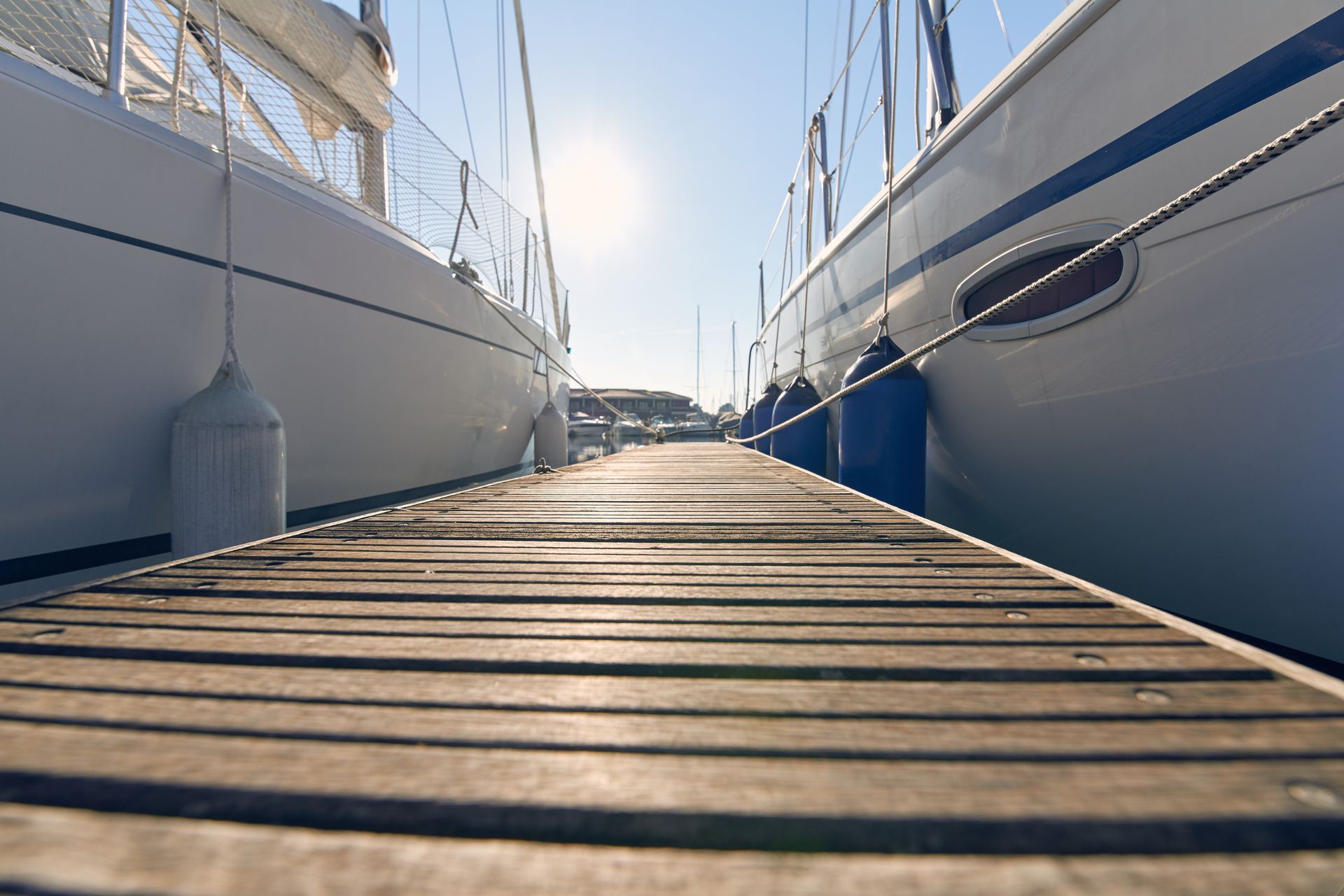 Wooden dock between two white sailboats at a marina, with the sun shining ahead. Wooden dock between two white sailboats at a marina, with the sun shining ahead.