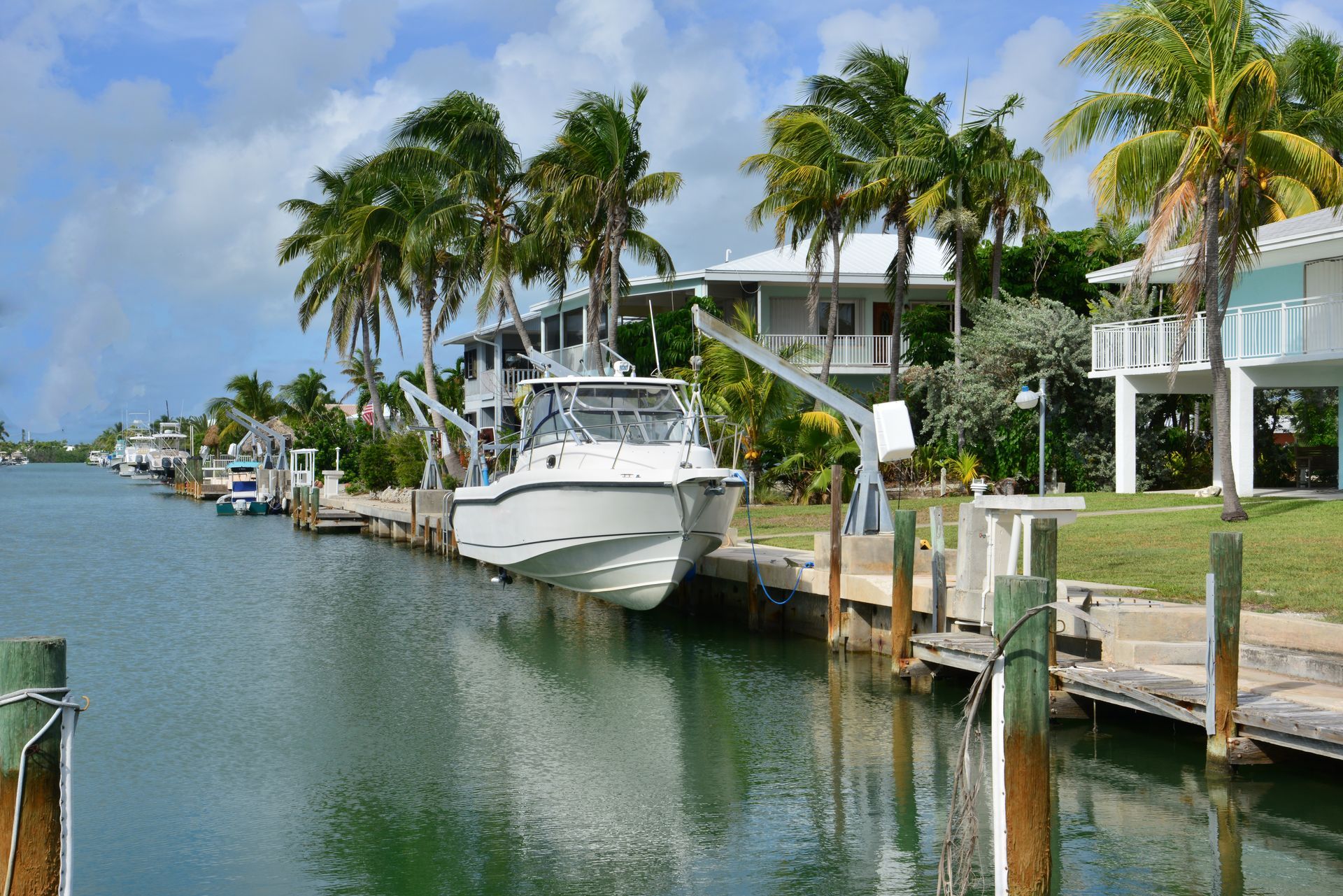White boat docked along a calm canal beside palm trees and waterfront homes on a sunny day White boat docked along a calm canal beside palm trees and waterfront homes on a sunny day