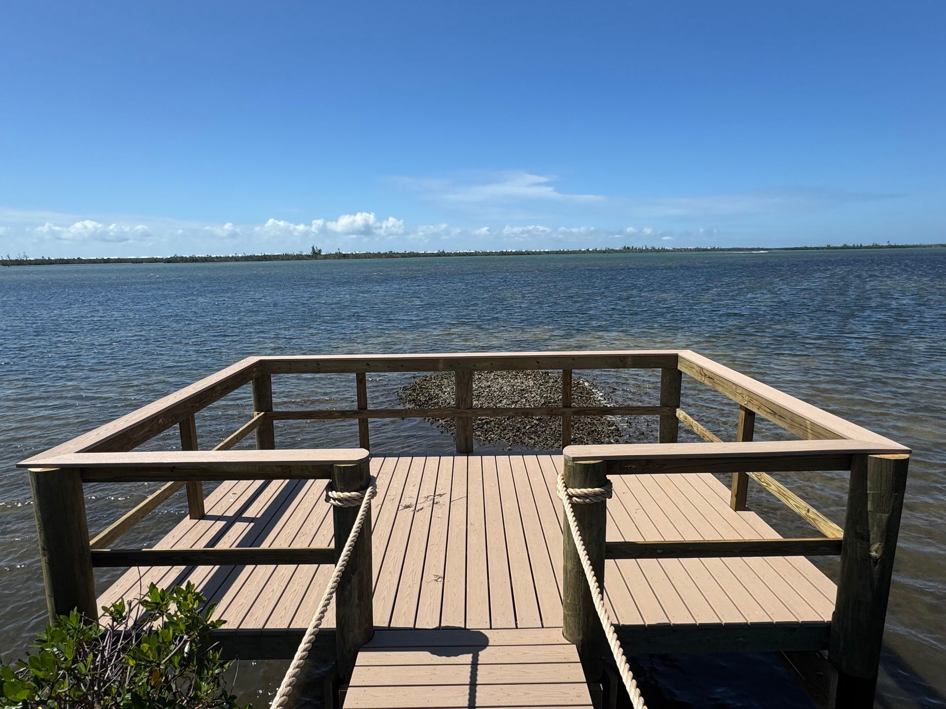 Wooden dock by calm water with boat, green posts, and a coiled hose on the right Wooden dock by calm water with boat, green posts, and a coiled hose on the right