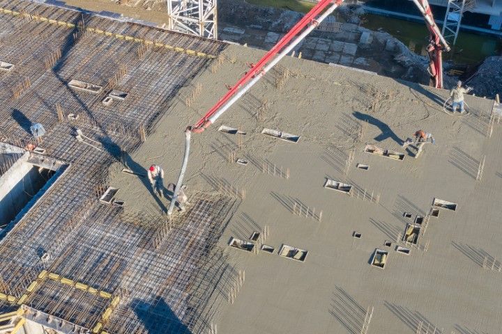 Construction workers pouring concrete on a large slab with a red boom pump