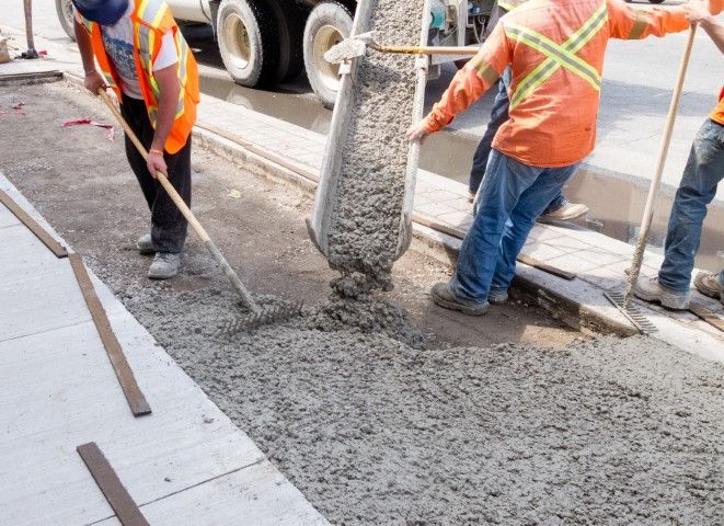 Road workers pouring wet concrete beside a truck on a street construction site