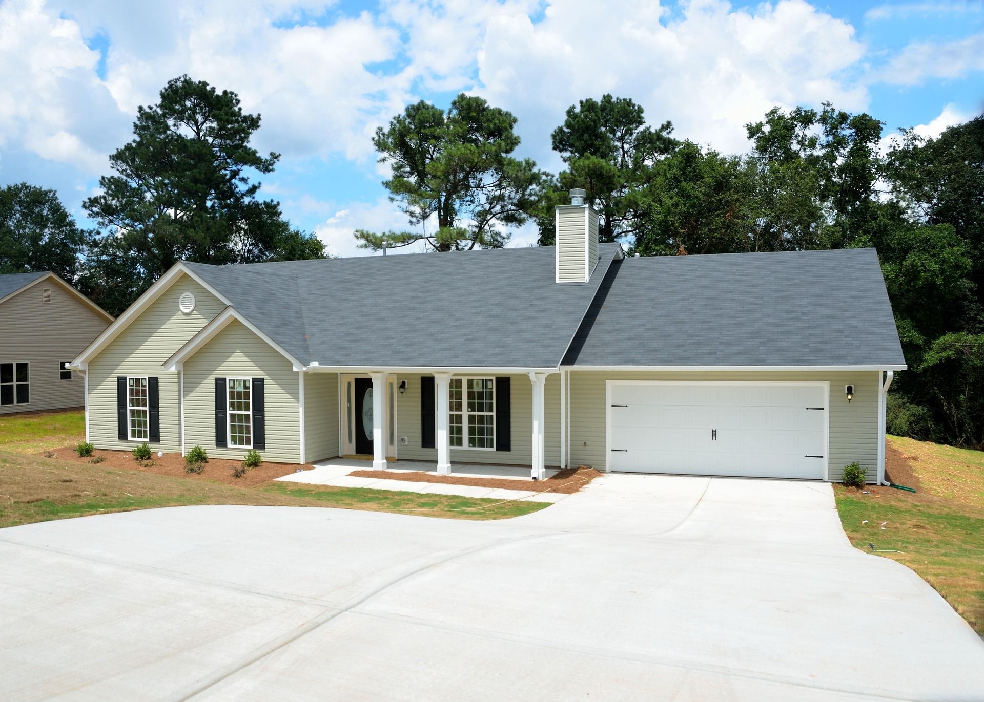 Single-story white house with gray roof, front porch, and attached garage on a sunny day