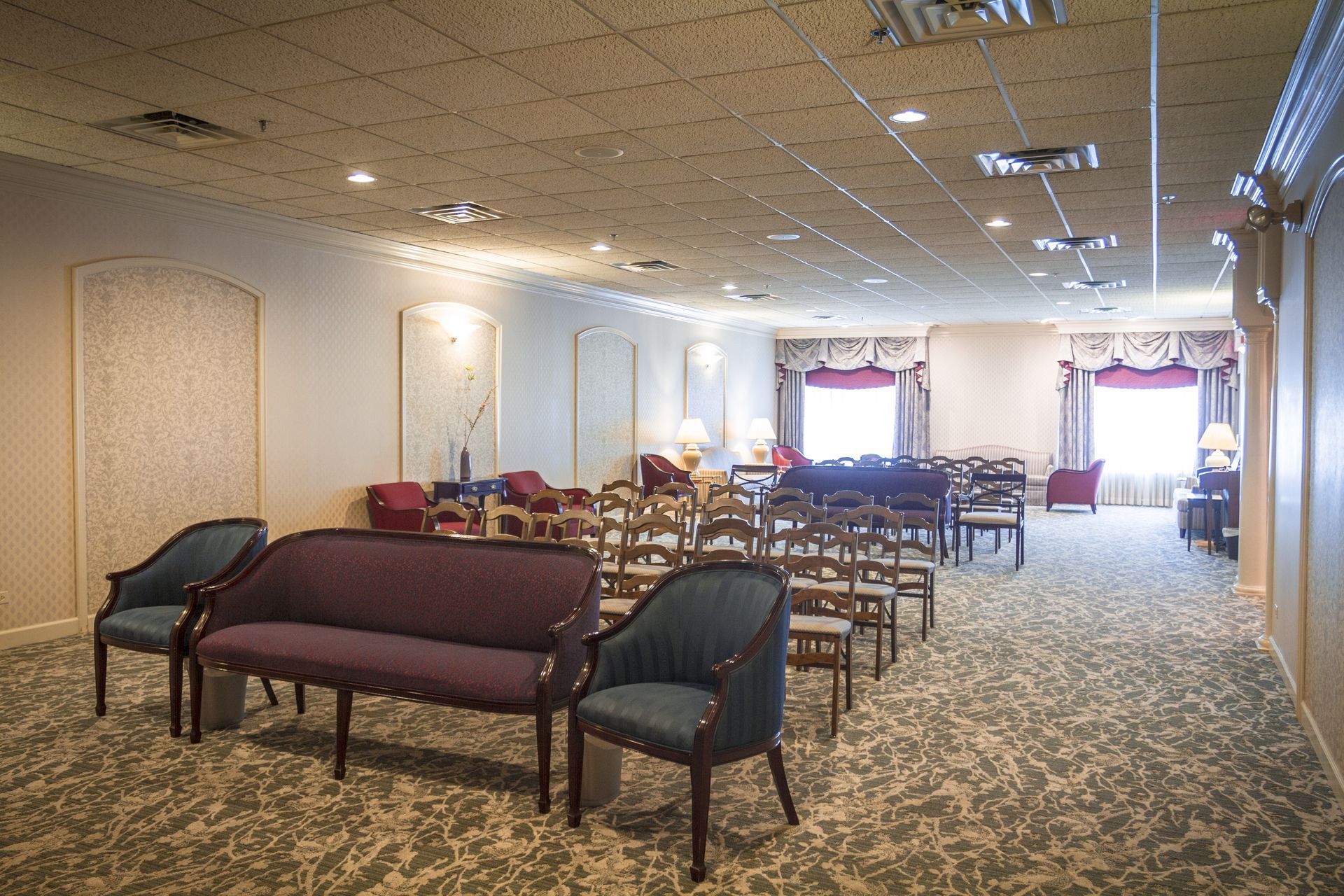 Empty banquet hall with rows of tables and chairs, patterned carpet, and bright windows at the far end
