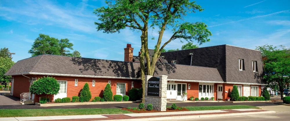 Brick office building with a dark roof, white trim, and a large tree along the street