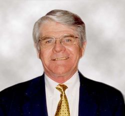 Studio portrait of a smiling man in a dark suit, white shirt, and gold tie on a light background