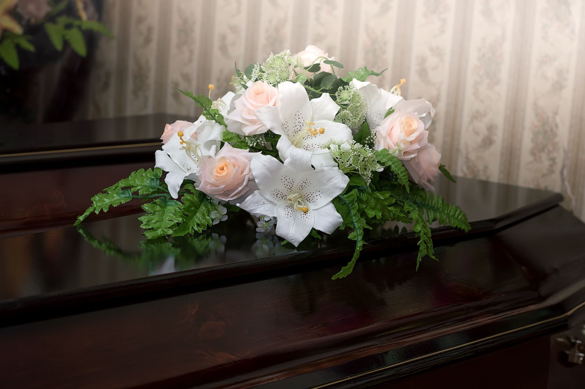White and pale pink flower bouquet on a polished dark piano against patterned wallpaper