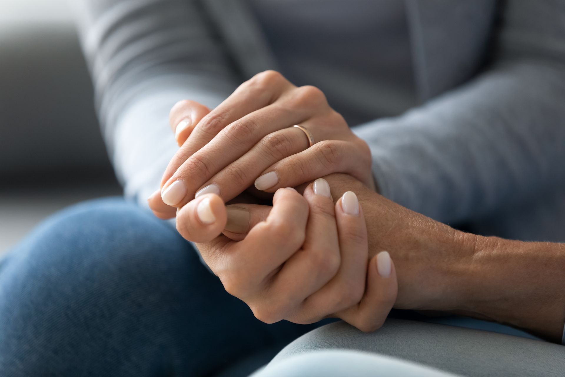Two hands clasped in a comforting gesture on a couch