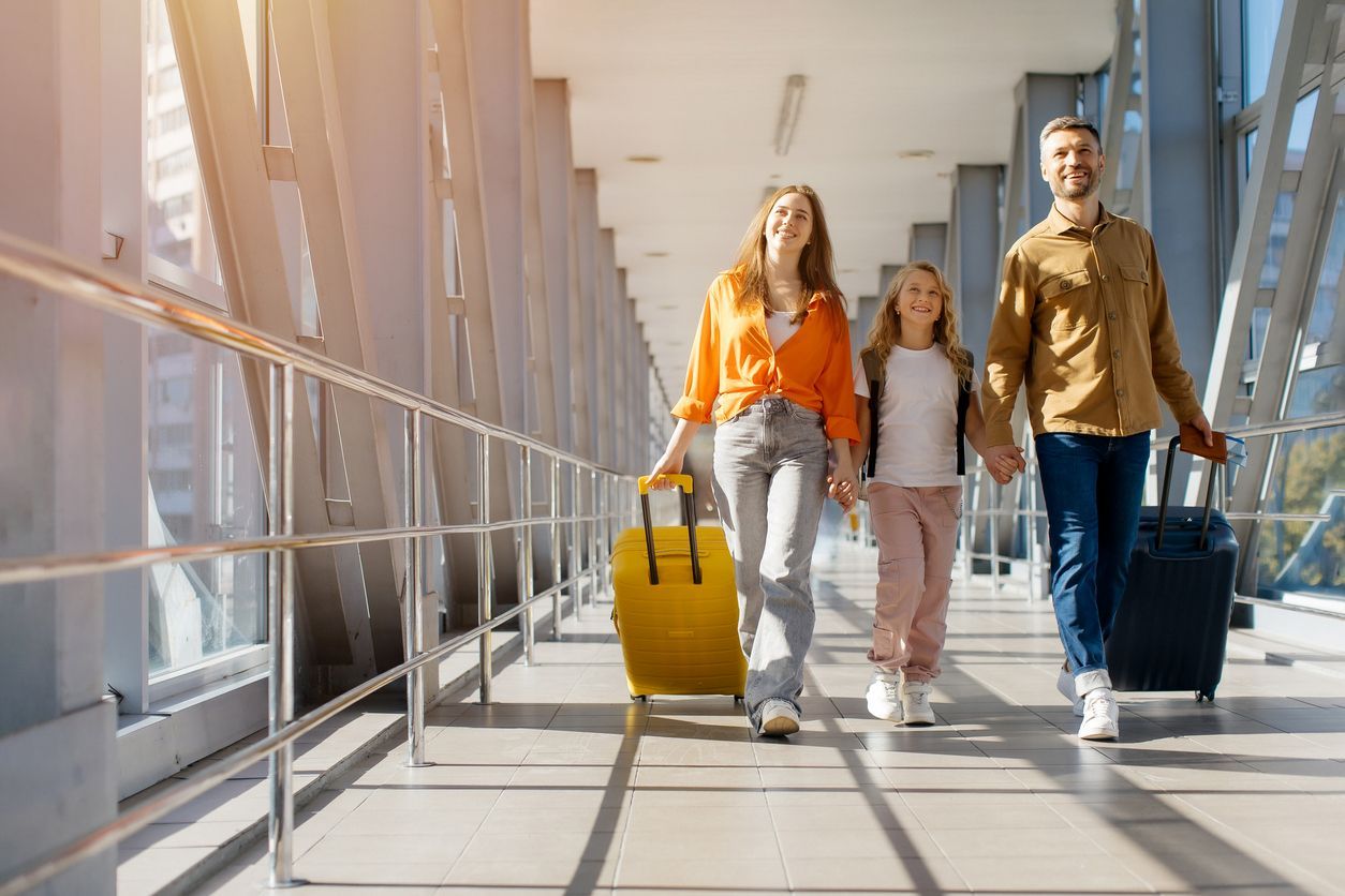 Three travelers walking through a bright airport corridor with rolling suitcases