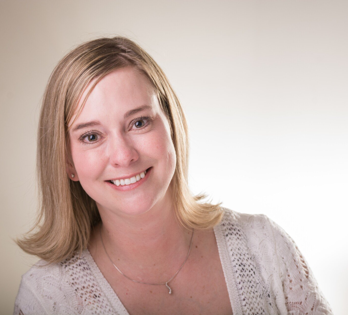 Smiling woman with blonde hair in a light knit top against a plain background