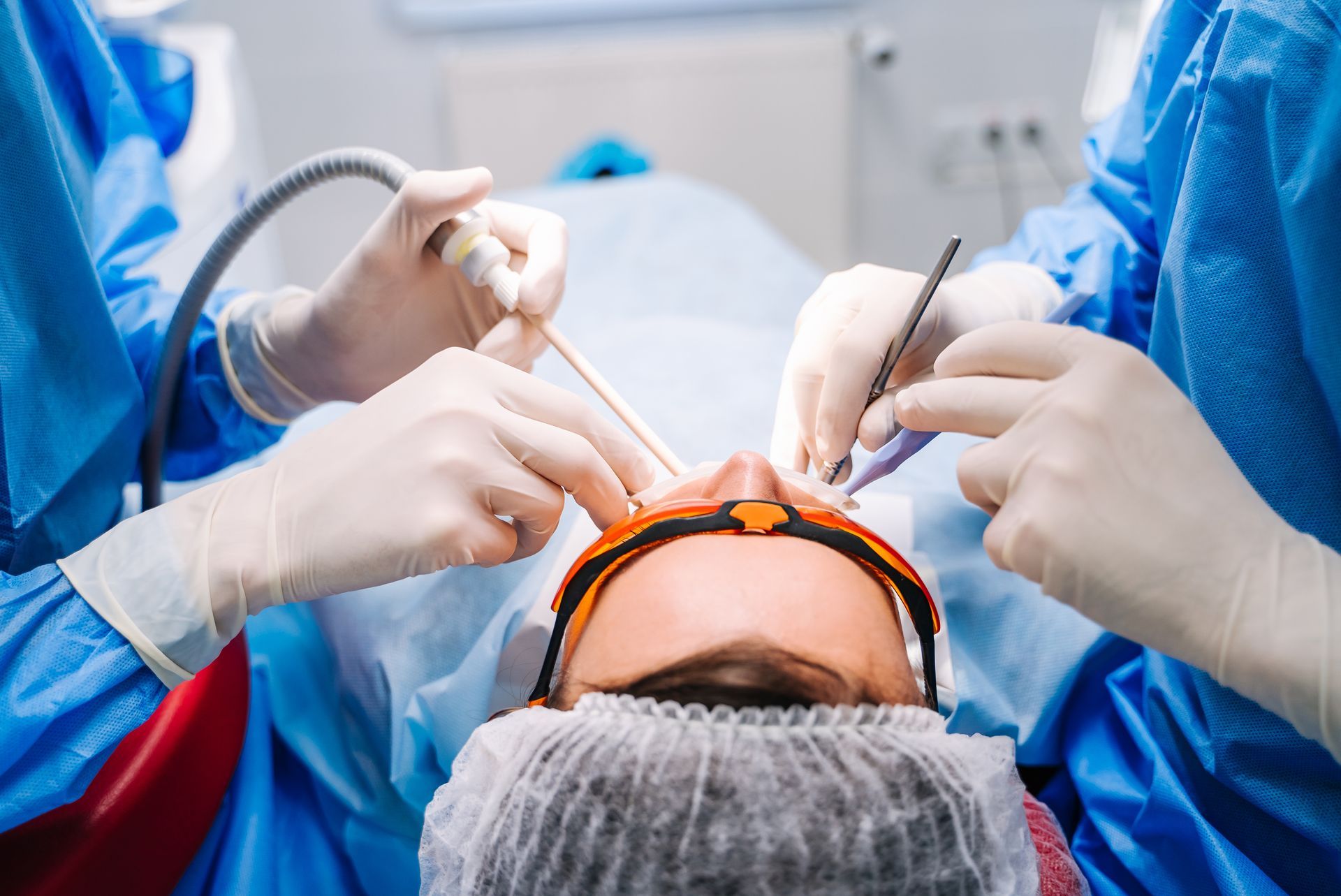 Dentist performing a procedure on a patient in a dental clinic, with gloved hands and tools visible.