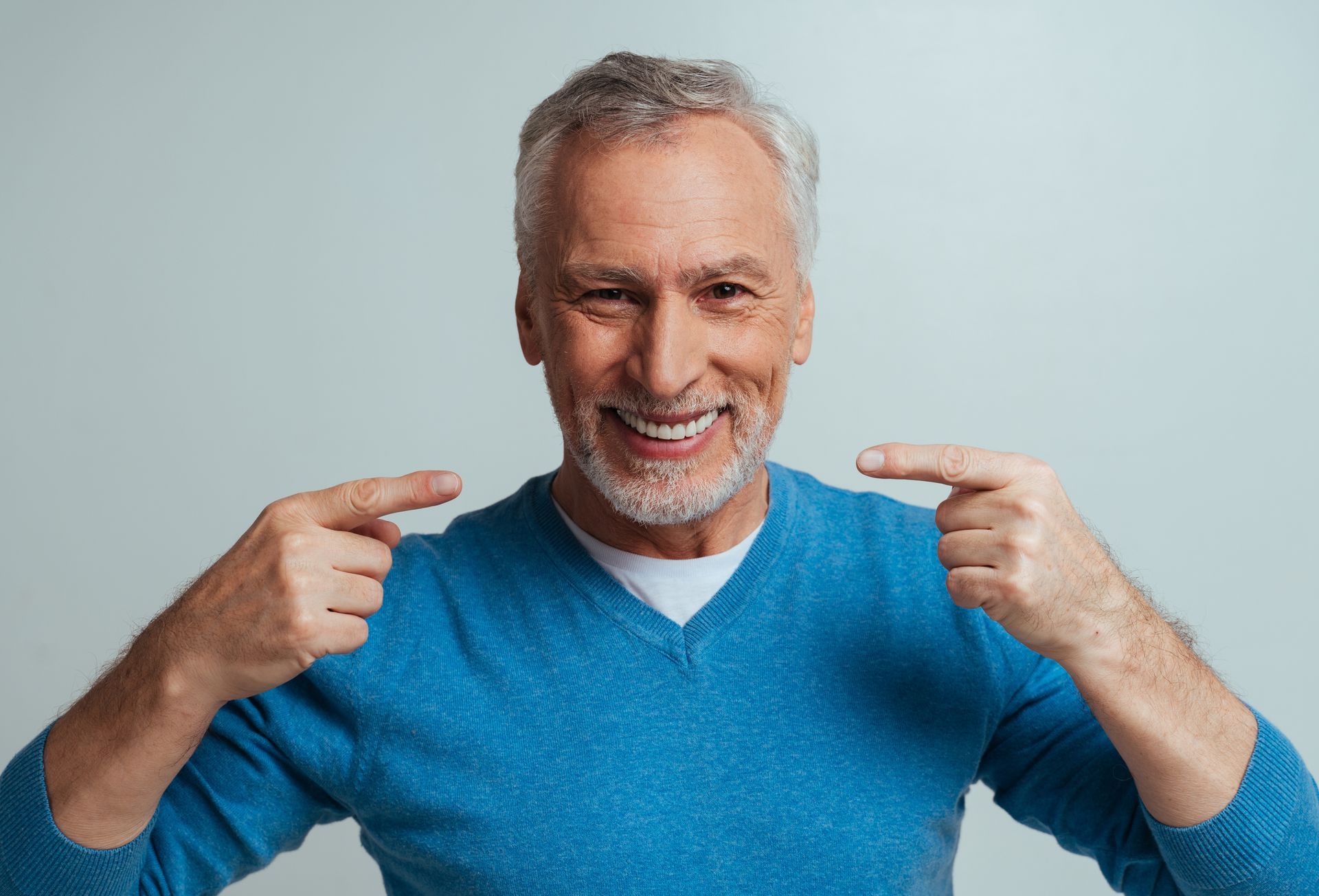 Smiling man in a blue sweater pointing at himself against a light gray background