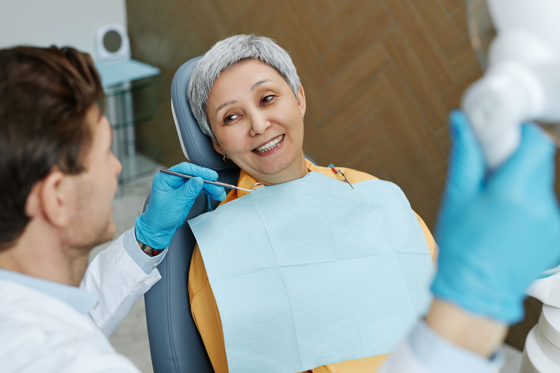 Dental patient smiling while receiving care, with gloved dentist and protective bib in clinic