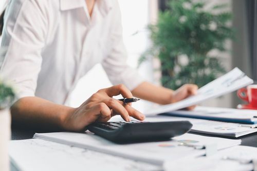 Person using a calculator at a desk with papers and a pen in an office setting