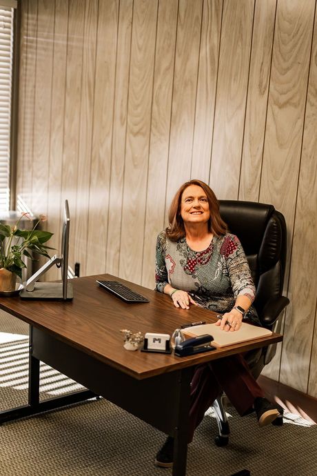 Woman smiling at a desk in an office, with a laptop, keyboard, and flowers beside her.