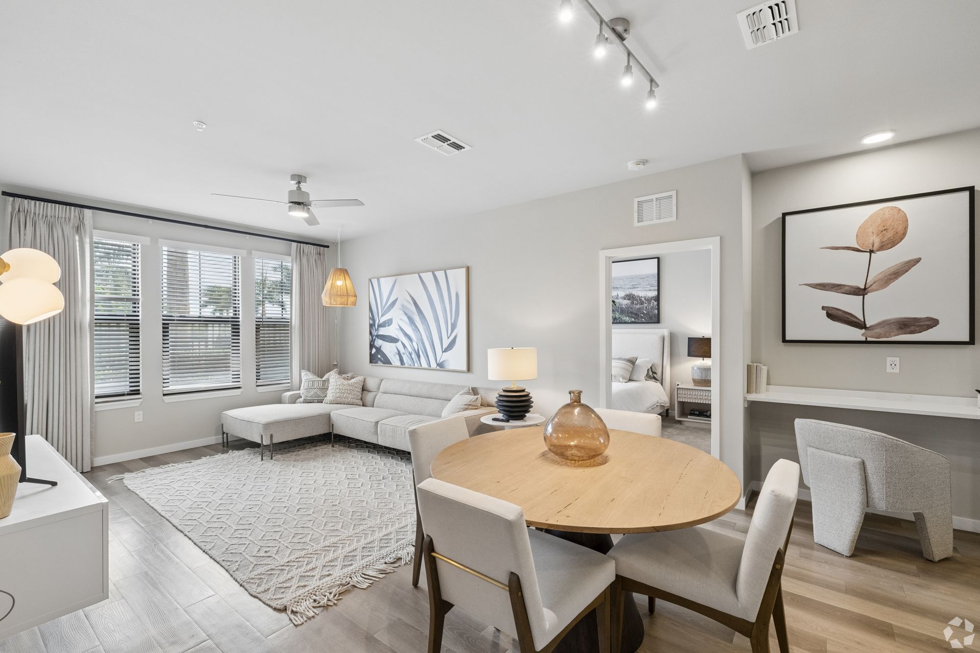 Bright modern living room and dining area with beige sofa, round table, wall art, and large windows.