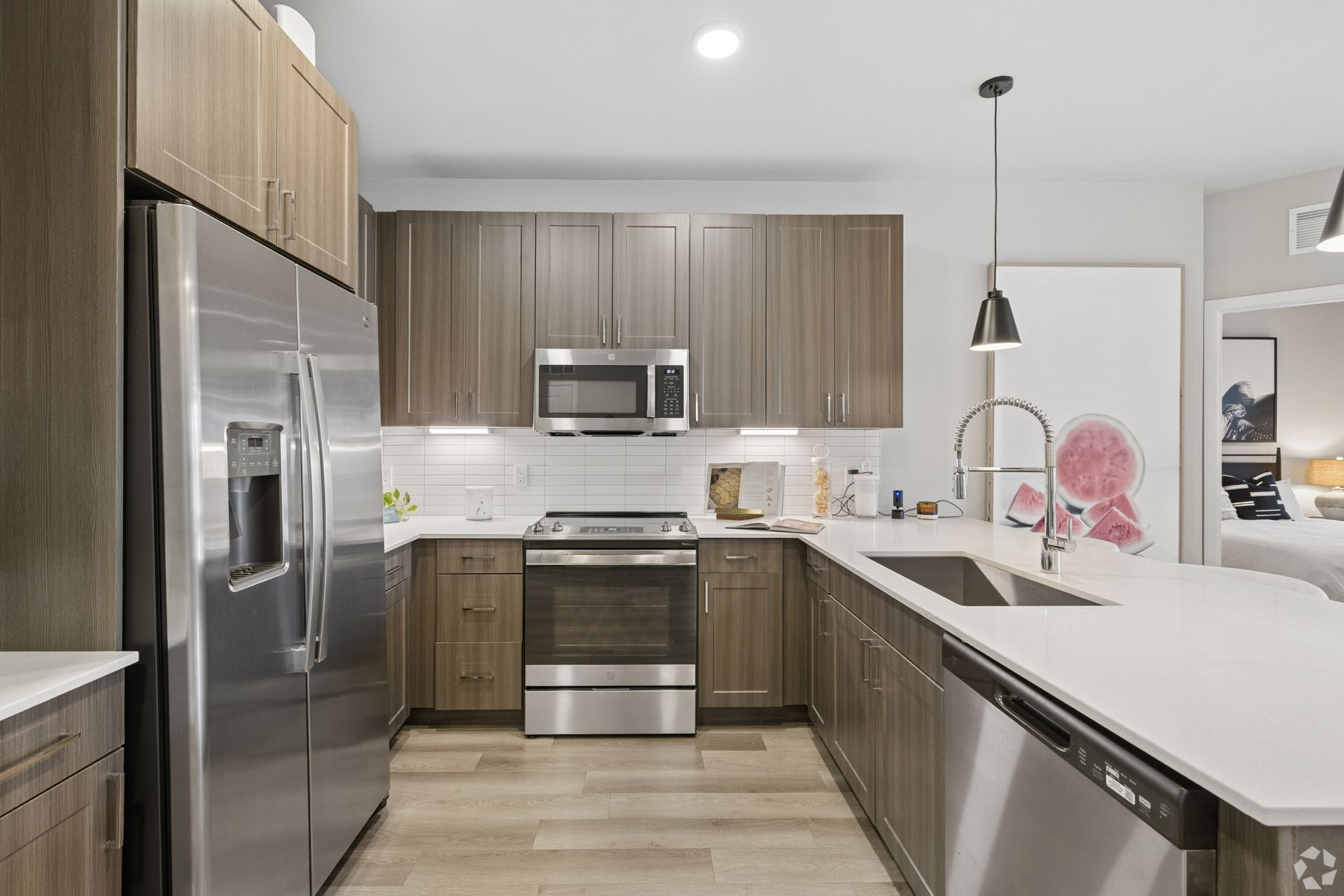 Modern kitchen with stainless steel appliances, gray cabinets, white counters, and a peninsula with pendant light.