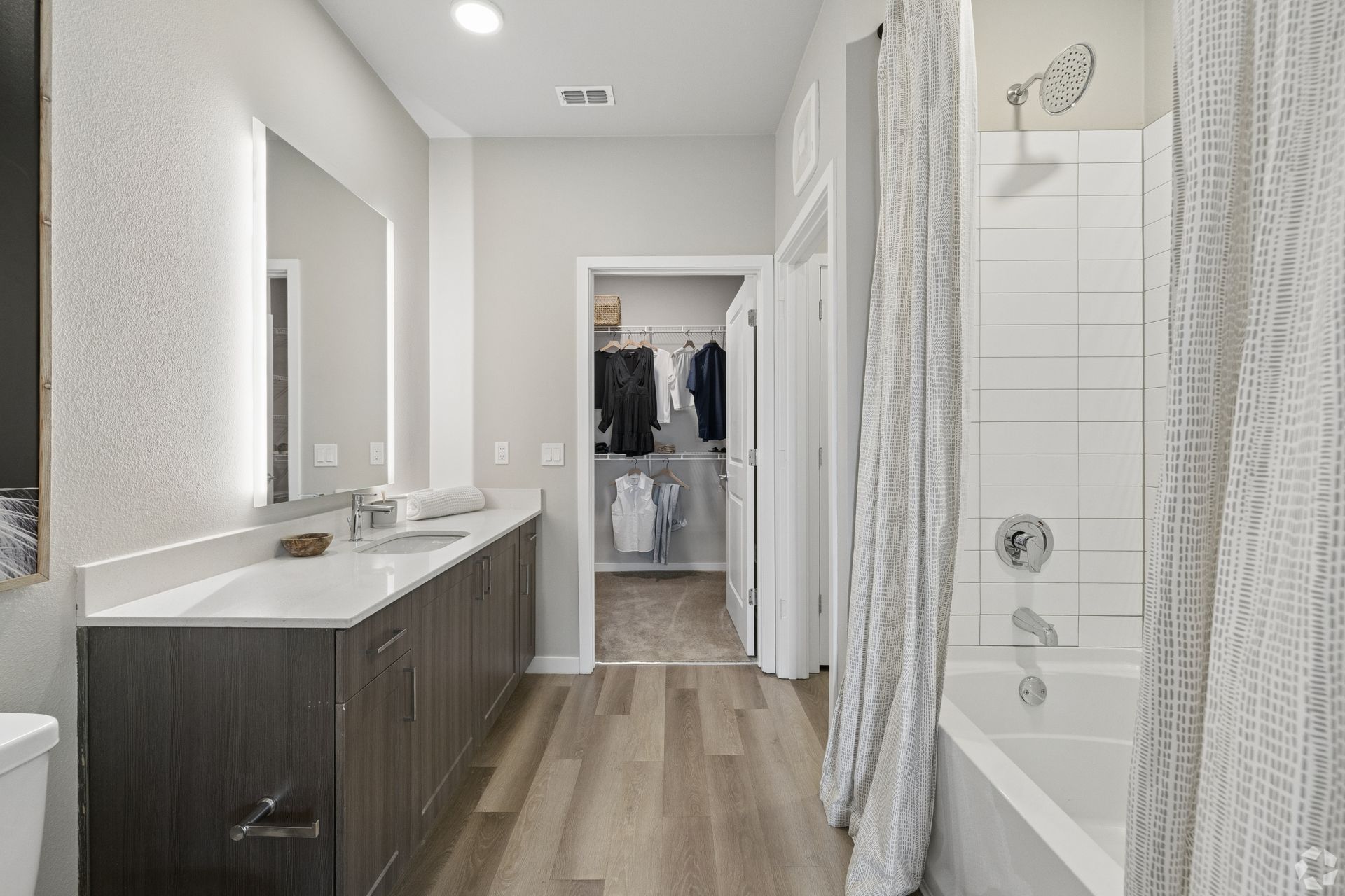 Modern bathroom with double vanity, walk-in shower, and open closet in the background