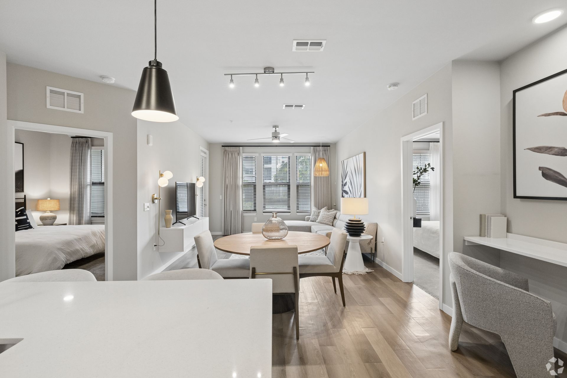 Bright modern open-concept apartment with white kitchen, dining area, gray seating, and wall art