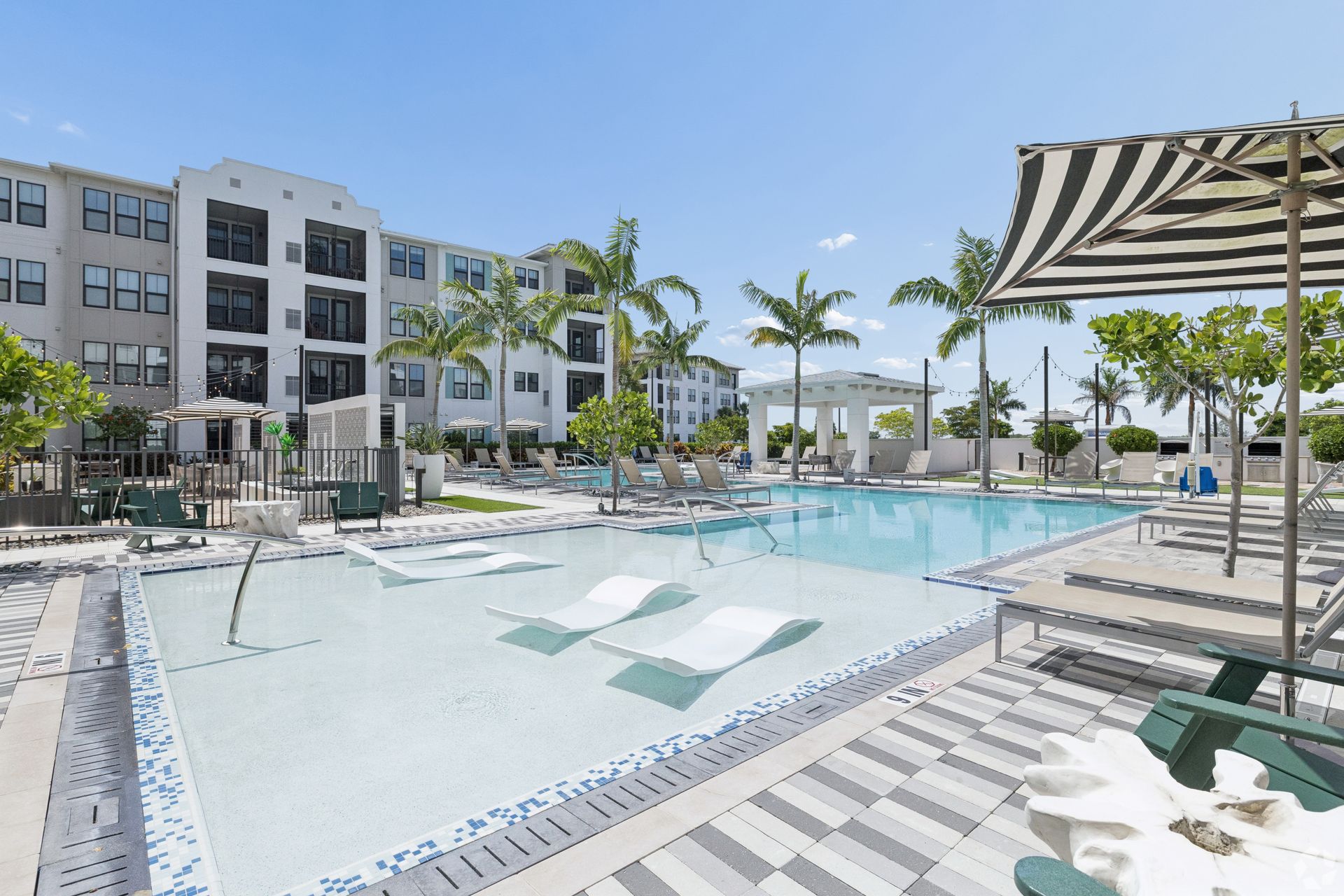 Modern apartment complex courtyard with a large turquoise pool, palm trees, and lounge seating