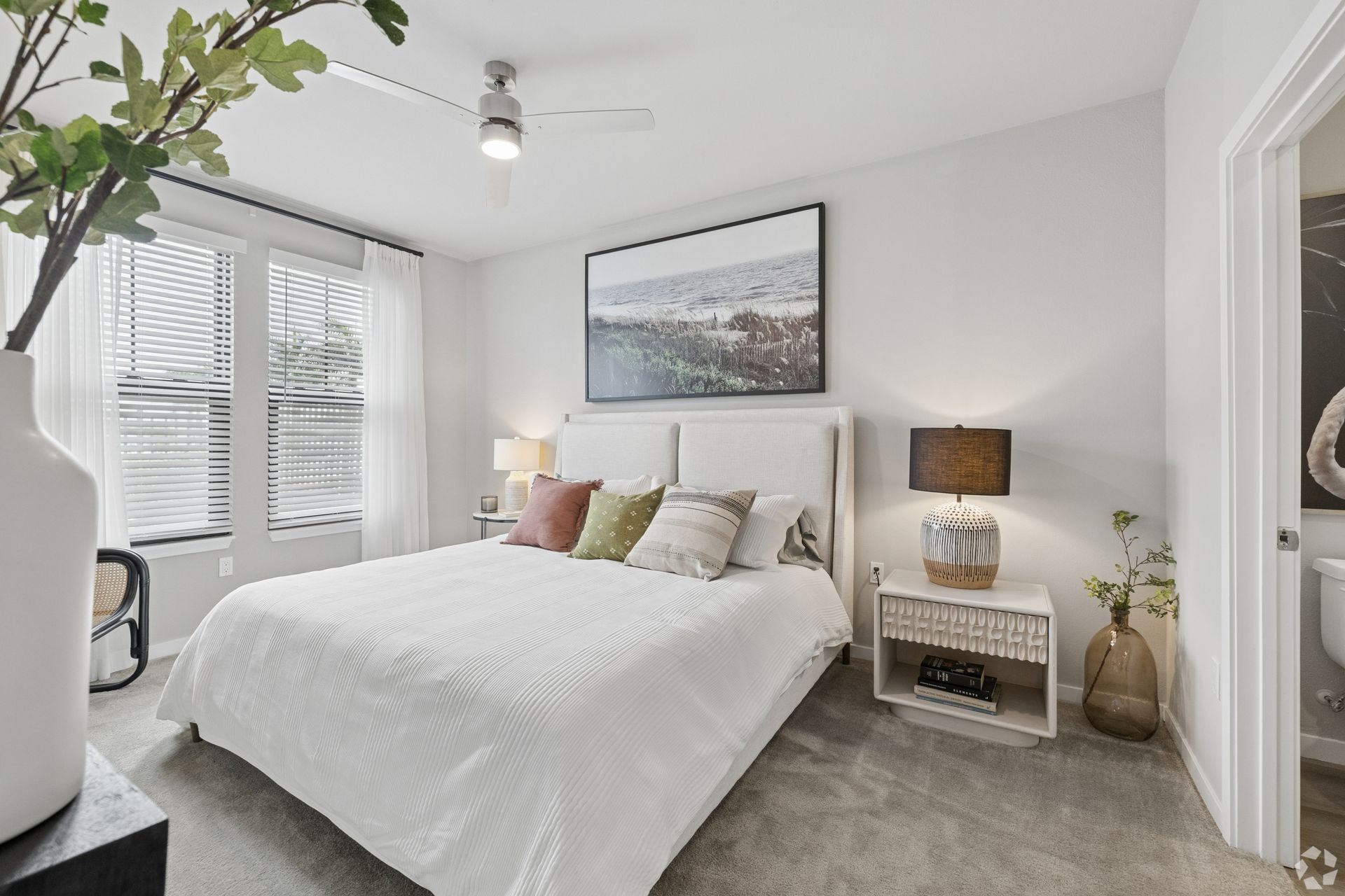 Bright bedroom with white bedding, bedside lamp, city wall art, and a window with blinds
