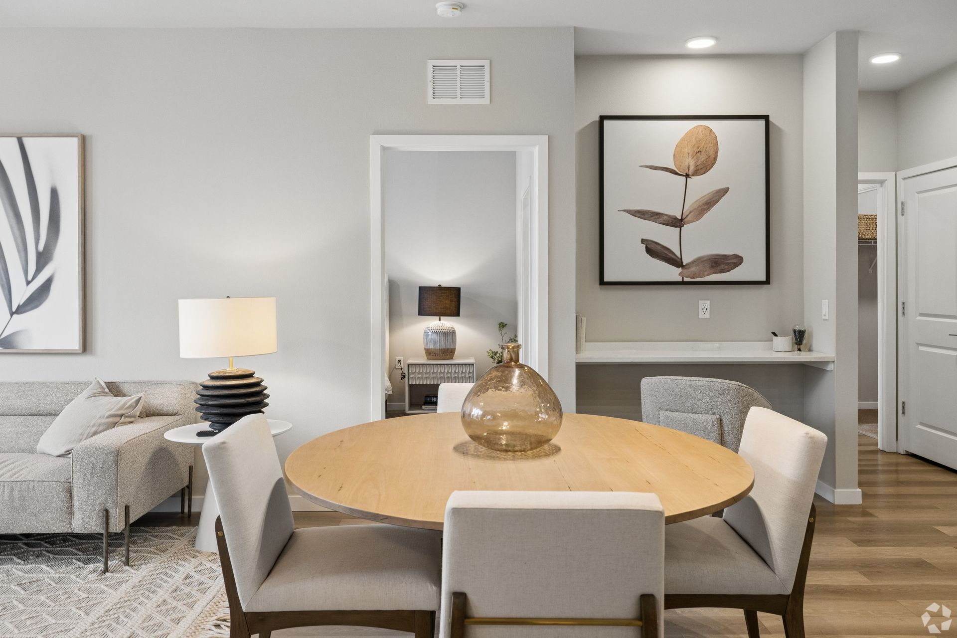 Modern dining room with round wooden table, white chairs, gray sofa, and floral wall art