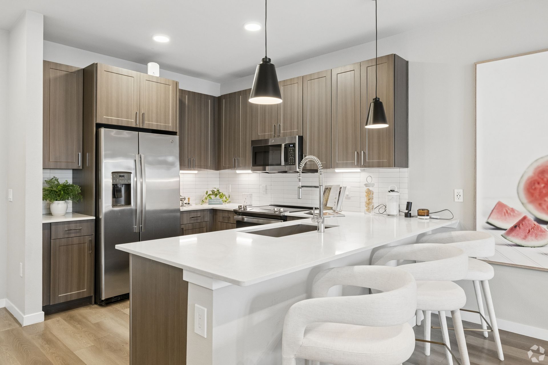 Modern kitchen with stainless steel appliances, white island, and bar stools under pendant lights