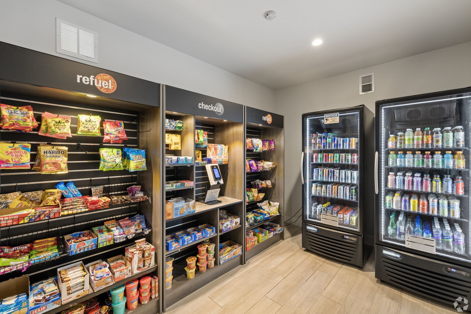 Convenience store snack aisle with shelves of chips and candy, plus refrigerated drink coolers.