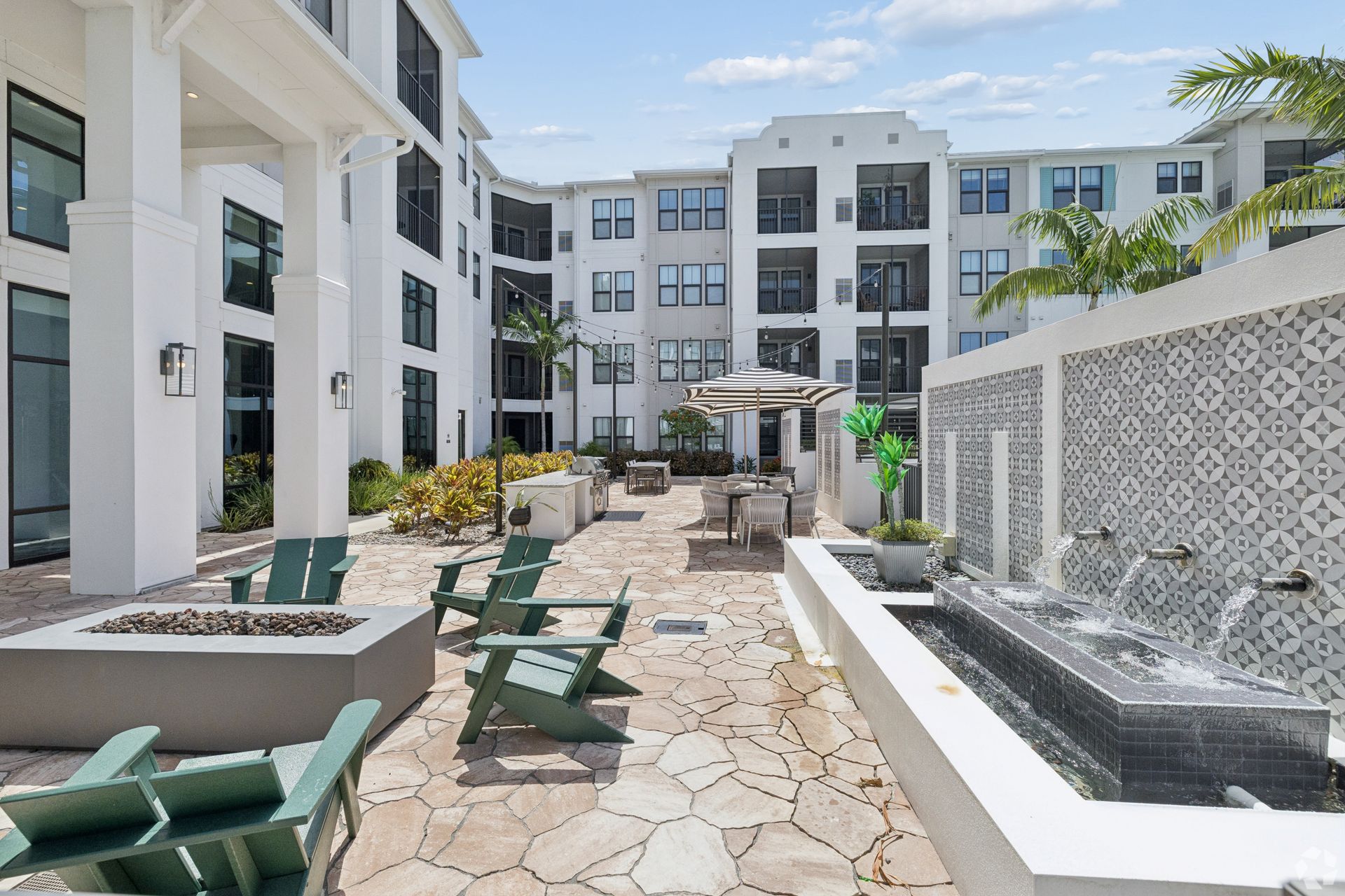Courtyard with lounge chairs, stone path, and fountain between modern white apartment buildings