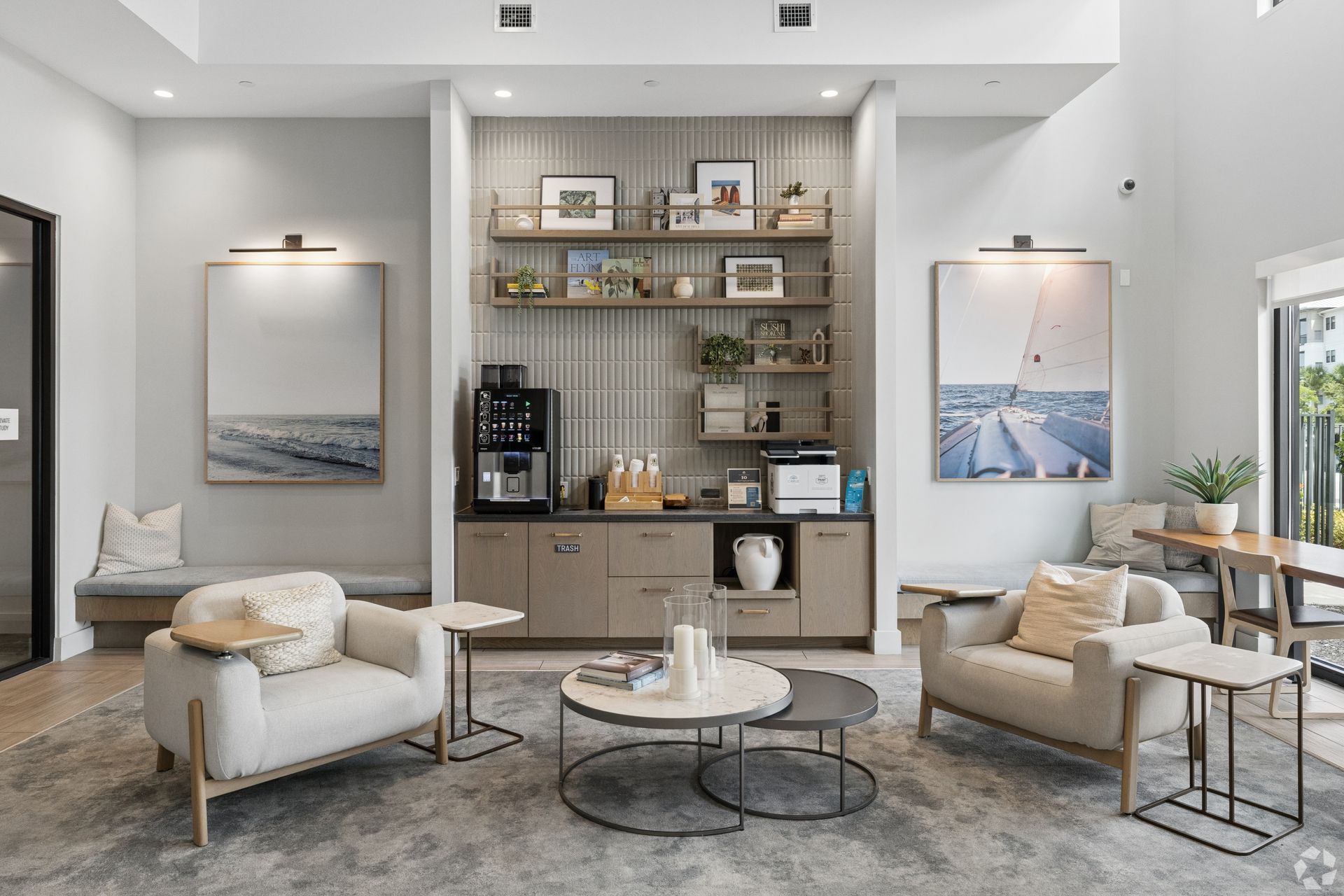 Bright modern living room with beige chairs, marble coffee tables, artwork, and built-in shelves