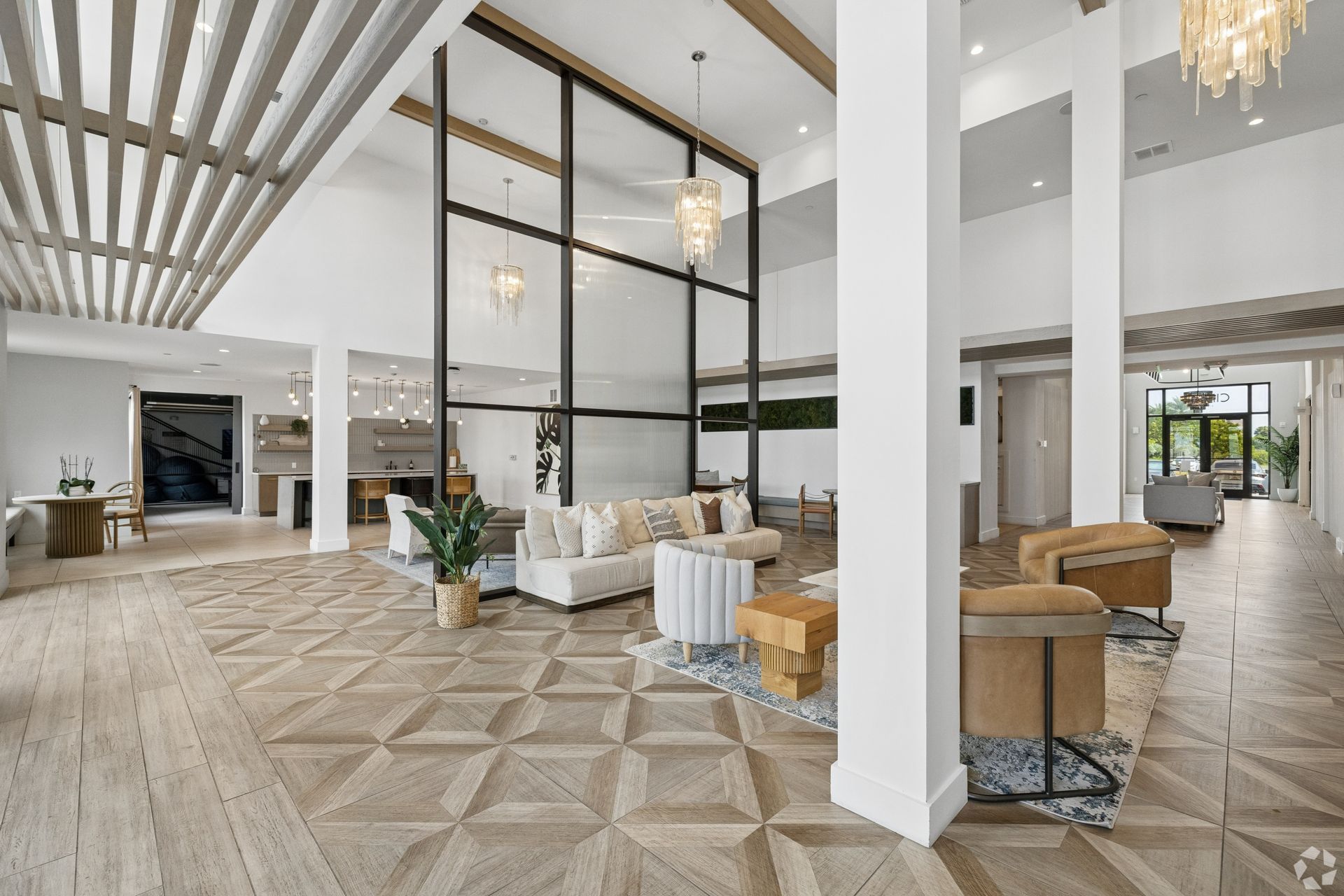 Modern hotel lobby with high ceilings, chandeliers, white columns, and patterned tile flooring
