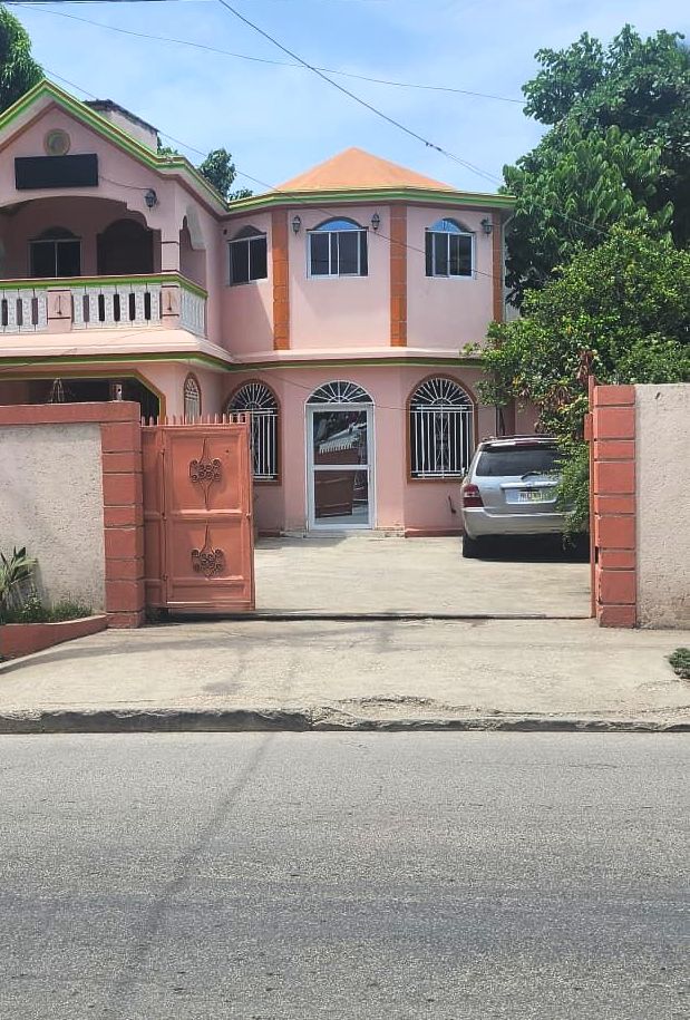 Pink two-story house with a car parked in the driveway behind a metal gate.