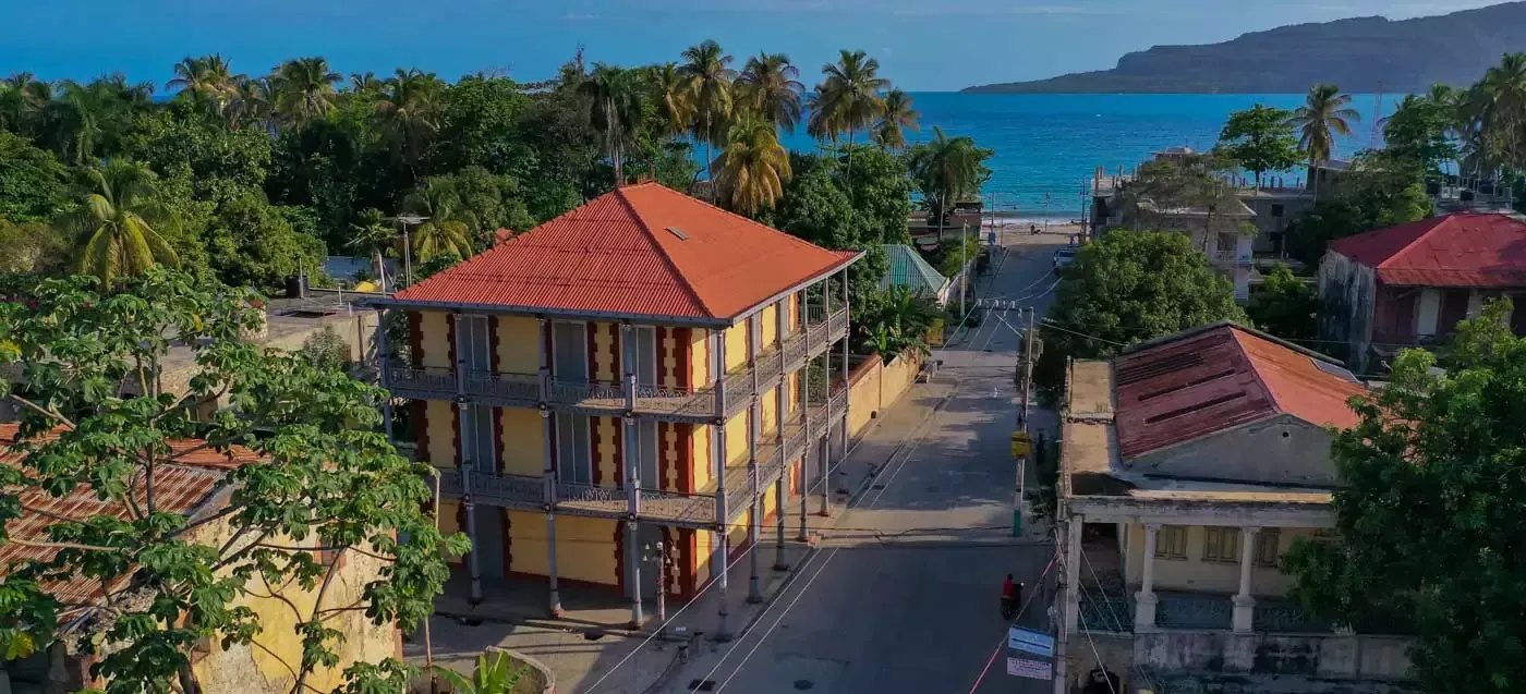 Coastal resort buildings with red roofs and palm trees overlooking a blue bay